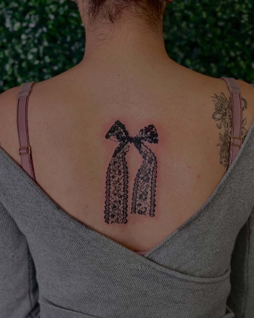 Delicate ribbon bow tattooed across the upper back